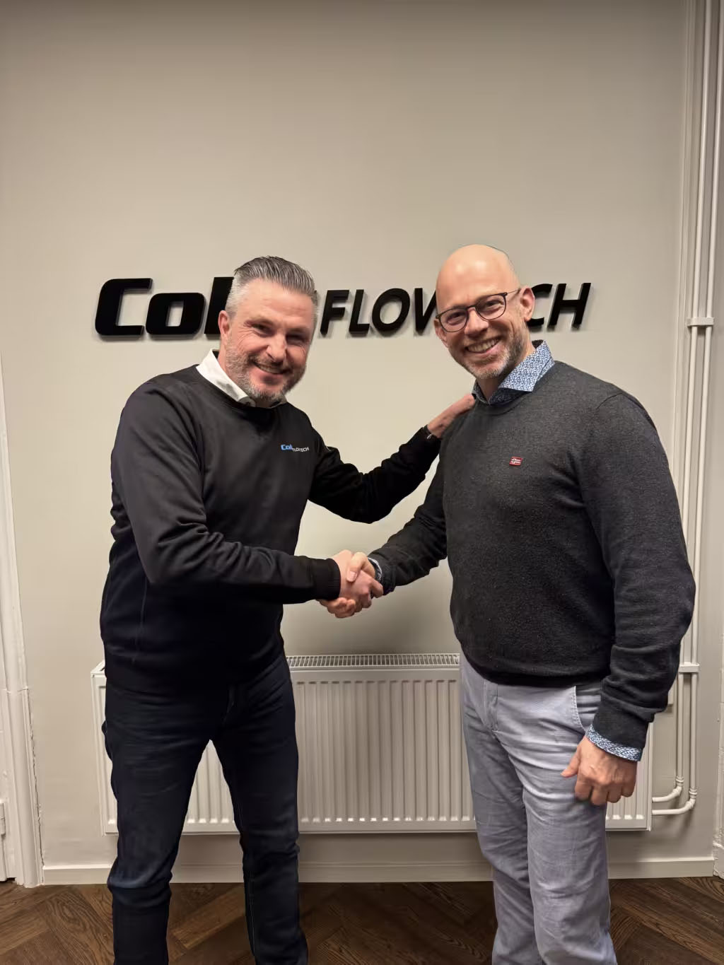 To mænd giver hånd foran et colly flowtech-skilt.
