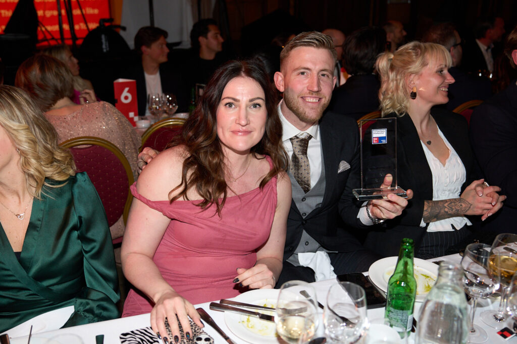 Rebecca Nilsson og Max Malm sidder ved middagsbordet til gallafesten med Great Place to Work-prisen i hånden og et smil på læben.