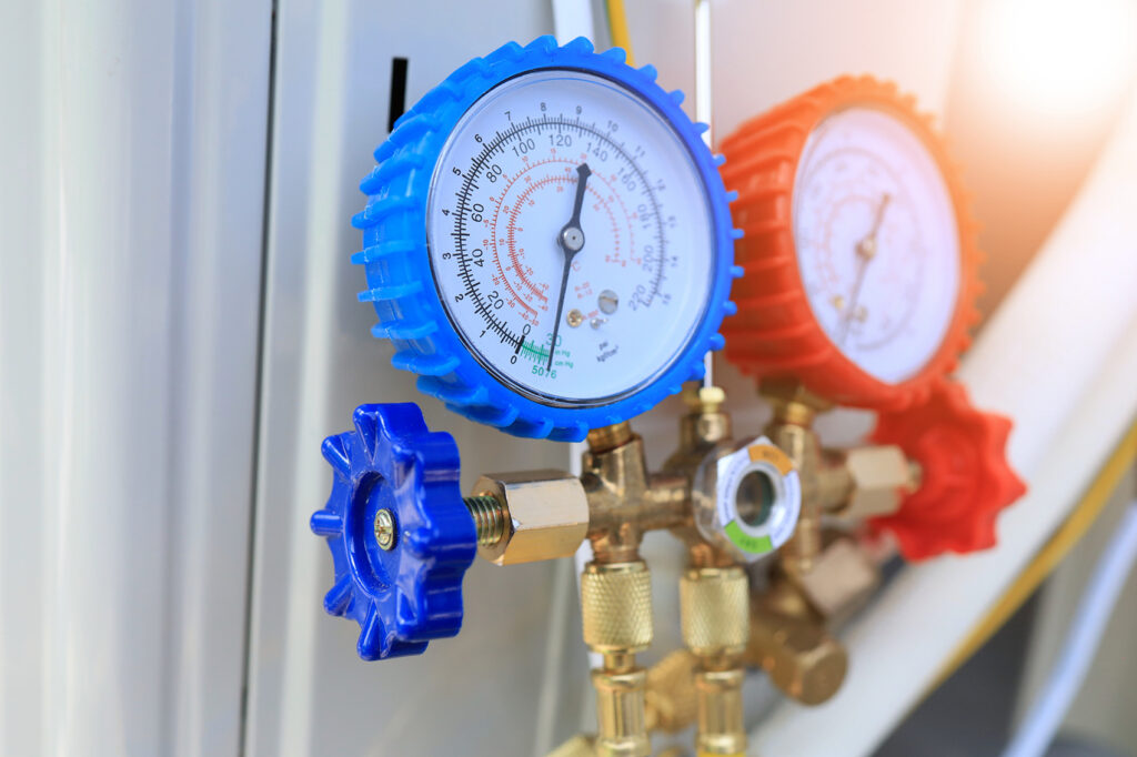 Nærbillede af et analogt manometerstativ med blå og rød måler til vakuum og tryk, monteret på et messingventilblok.